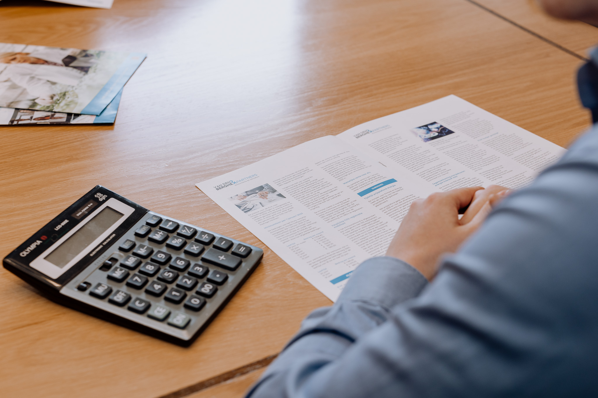 Man bekijkt financiële brochure aan tafel met rekenmachine ernaast.