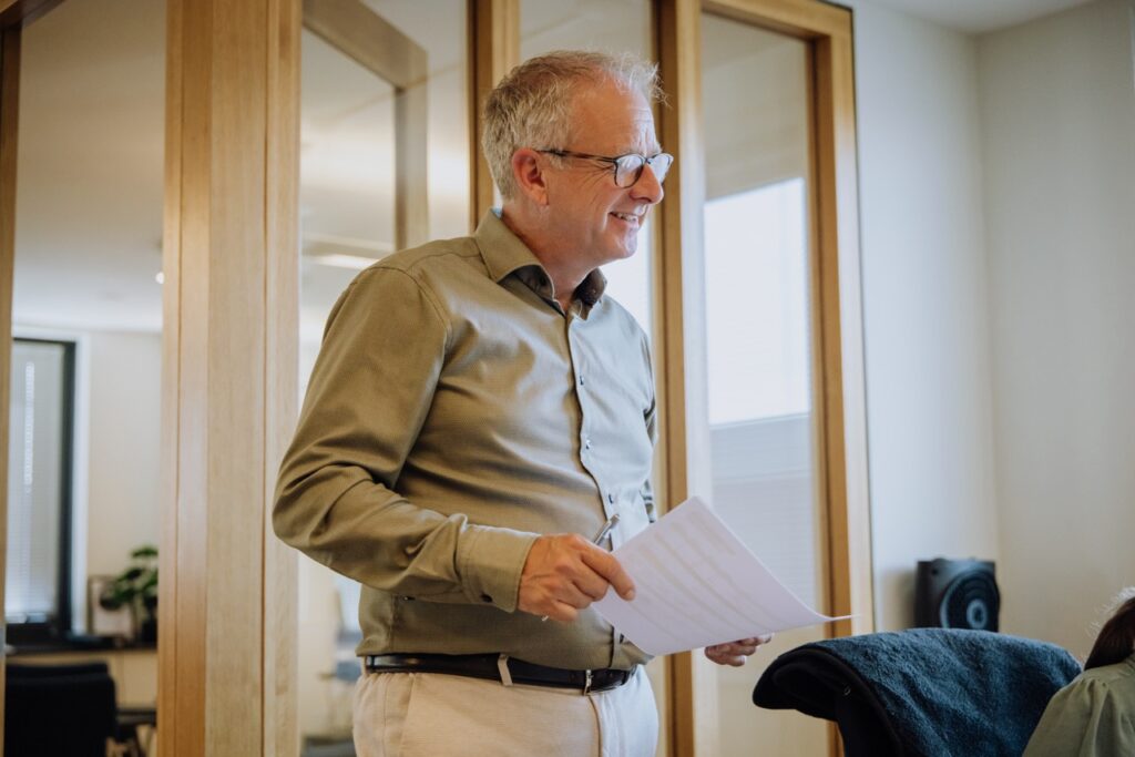Man geeft uitleg terwijl hij een document vasthoudt in een moderne kantoorruimte met houten kozijnen.