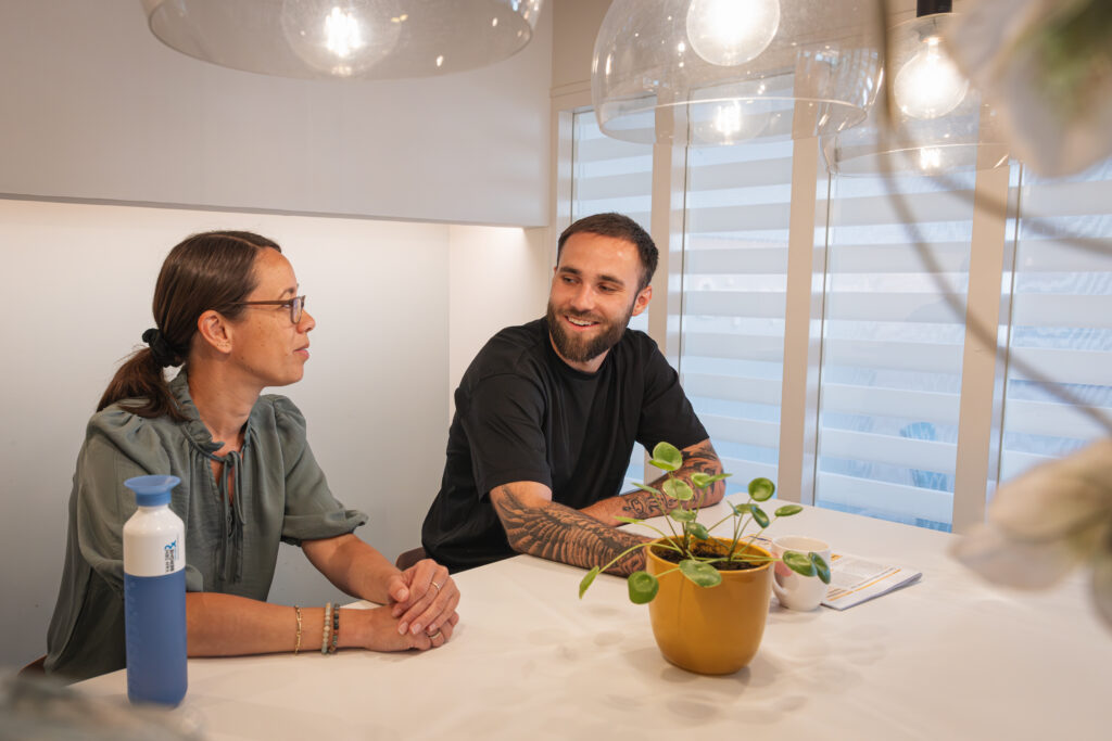 Twee collega’s in gesprek aan een vergadertafel met planten en warme verlichting, tijdens een informele bespreking bij Van den Berghe & Partners.