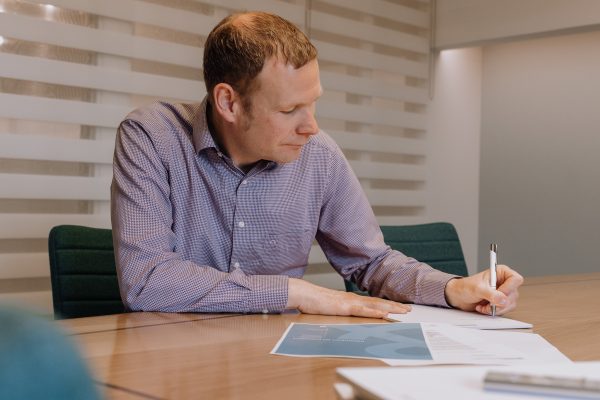 Man aan een bureau die documenten bekijkt en aantekeningen maakt.