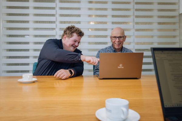 Twee collega’s bespreken iets enthousiast op een laptop aan een vergadertafel, met focus op samenwerking en plezier.