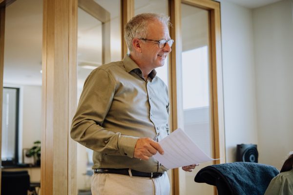 Man geeft uitleg terwijl hij een document vasthoudt in een moderne kantoorruimte met houten kozijnen.